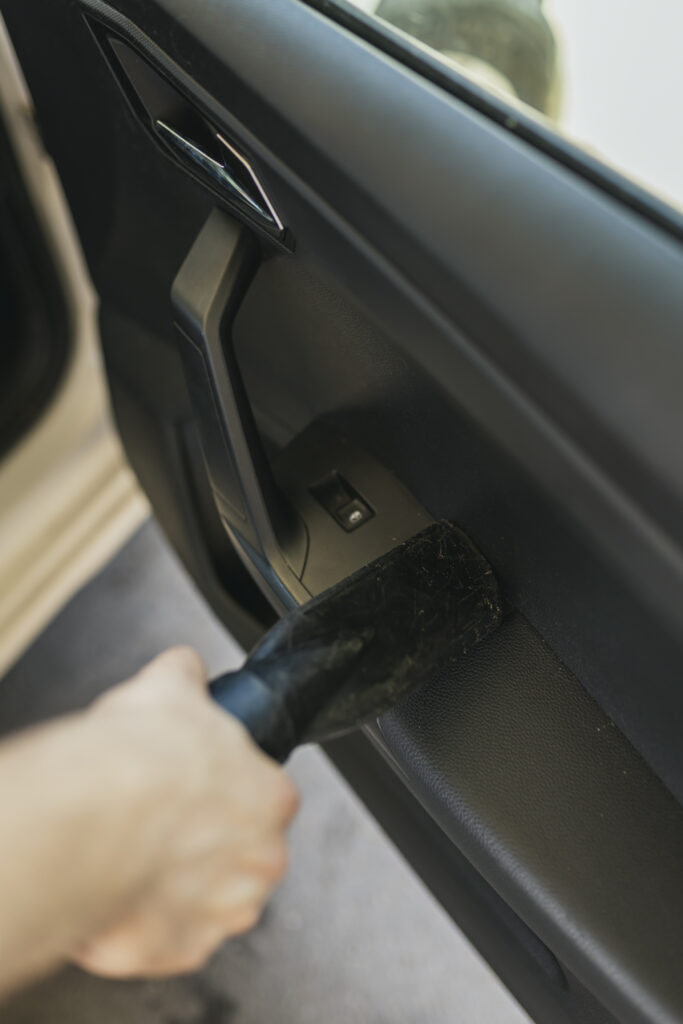 Primer plano de una mano utilizando la boquilla de un aspirador para limpiar el interior de la puerta de un coche negro en Gasolinera Teckmar