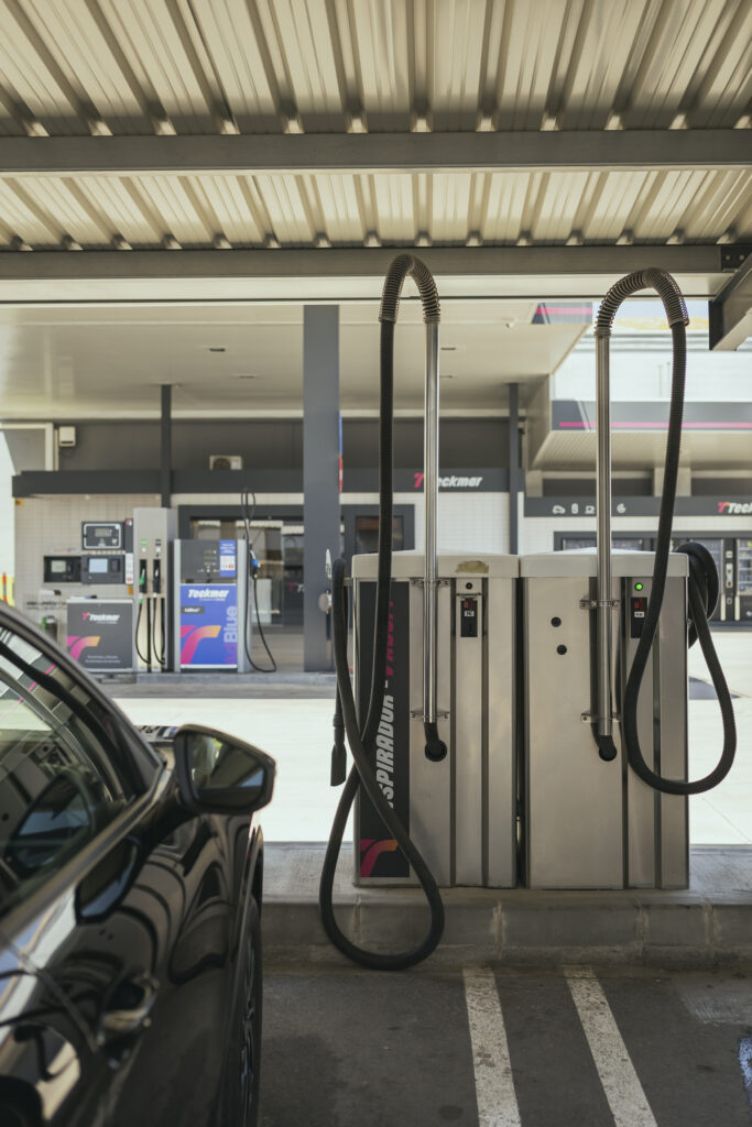 Dos máquinas de aspirado de coches de acero inoxidable bajo una carpa metálica en la zona de limpieza de la Gasolinera Teckmar, con un coche negro estacionado en primer plano.