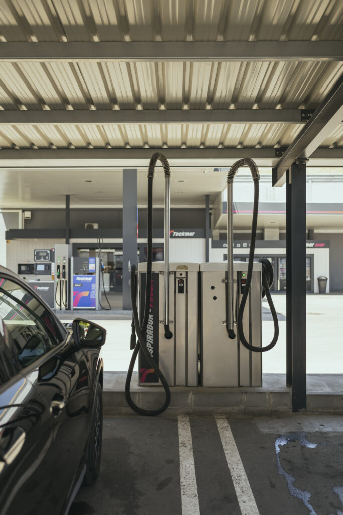 Dos máquinas de aspirado de coches de acero inoxidable bajo una carpa metálica en la zona de limpieza de la Gasolinera Teckmar, con un coche negro estacionado en primer plano.