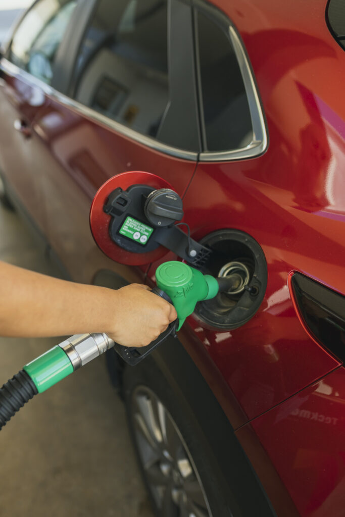 Primer plano de una mano introduciendo un boquerel verde de gasolina en el depósito abierto de un coche rojo en la Gasolinera Teckmar